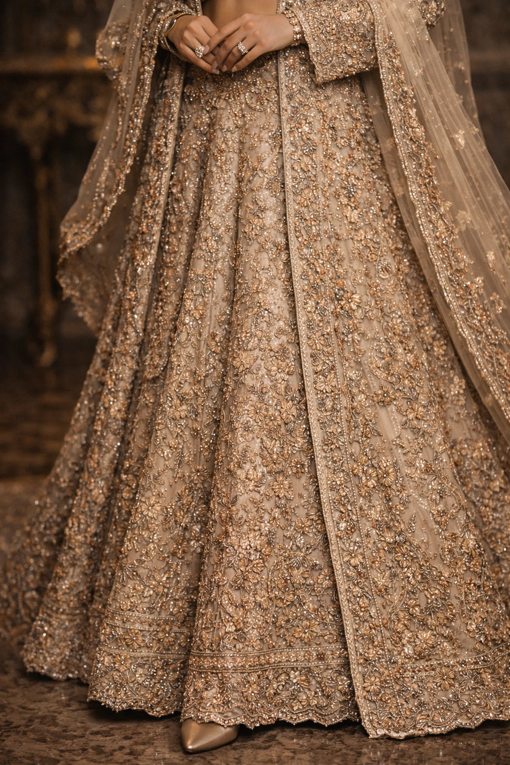 Bride wearing champagne embroidered bridal lehenga with long jacket and sheer dupatta in royal interior setting